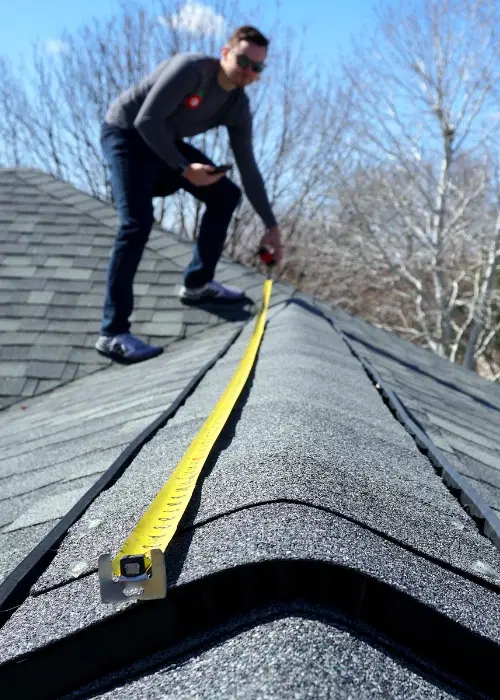 Roofer working on top of roof with tape measurer